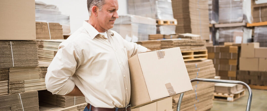 Side view of worker with backache while lifting box in the warehouse