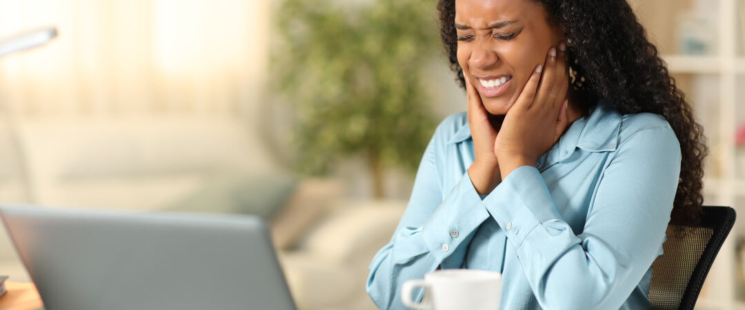 A woman holds her jaw in her hands easing her TMJ pain