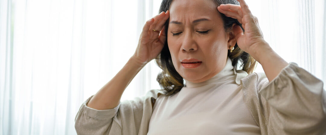 An unwell older woman suffers from vestibular pain while holding her temples